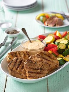 grilled pork chops and vegetables on a plate with dipping sauce in the middle