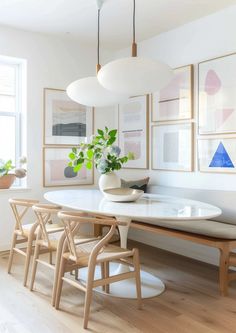 a dining room table and chairs with art on the wall behind it in front of a window