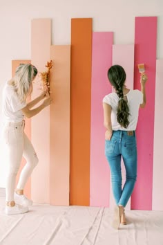 two women are standing in front of colorful walls and one is painting the wall with her hands