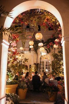 people are sitting at a table in the middle of an archway with potted plants