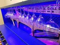 several wine glasses are hanging from the ceiling in front of a blue shelf with purple lights