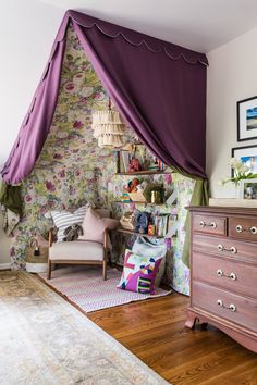 a bedroom with a purple canopy and floral wallpaper on the walls next to a dresser