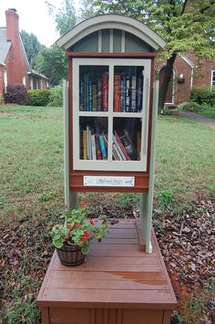 a display case with books on it in the middle of a yard next to a tree