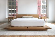 a bed sitting on top of a wooden platform in a bedroom next to two windows