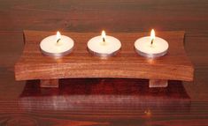 three white candles sitting on top of a wooden stand with four lit ones in the middle