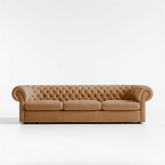 a tan leather couch with buttons on the armrests and back rests against a white wall