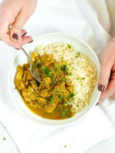 two hands are holding a fork over a bowl of rice and meat with gravy