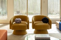 two yellow chairs sitting next to each other in a living room with large glass windows