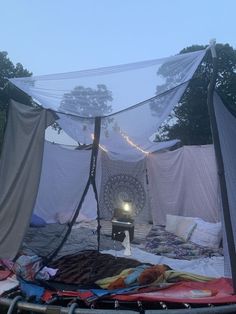 an outdoor tent is set up with mosquito netting and lights on the ground, in front of trees