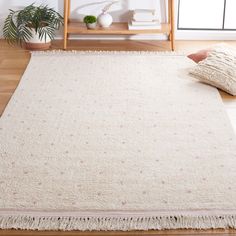 a white rug with fringes on the floor in front of a wooden shelf and potted plant