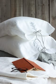 a stack of white pillows sitting on top of a bed next to a pair of glasses