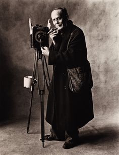 an old black and white photo of a man holding a camera next to a tripod