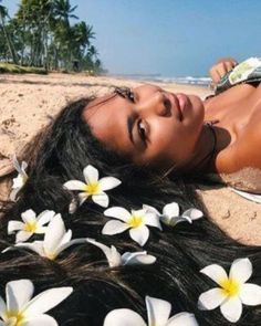 a woman laying on the beach with flowers in her hair