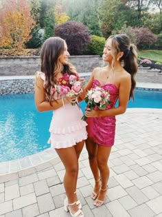 two beautiful young women standing next to each other near a pool with flowers in their hands