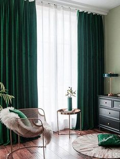 a living room with green drapes and wooden flooring, two chairs in front of the window