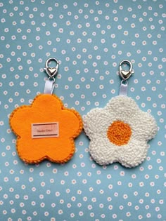 two flower shaped key chains on a blue and white background with tiny flowers in the center