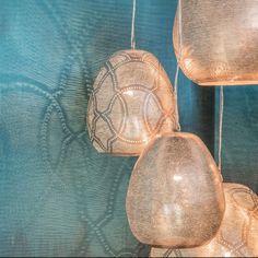 three lamps hanging from strings in front of a blue wall with an intricate pattern on it