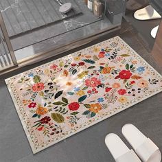 a bathroom rug with flowers on it next to two white slippers and a toilet