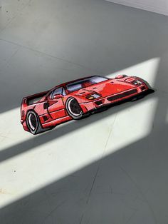 a red toy car sitting on top of a white floor next to a shadow cast wall