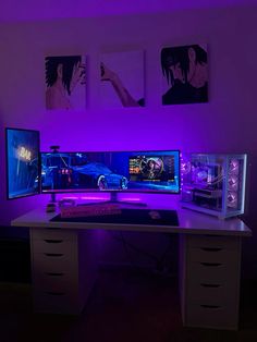 two computer monitors sitting on top of a desk in front of purple lights and pictures