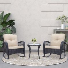 two chairs and a table on a rug in front of a white wall with potted plants