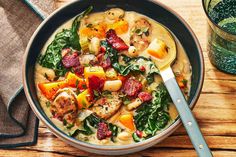 a bowl of soup with spinach, sausage and other vegetables on a wooden table