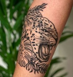 a black and white tattoo of a leopard on the left arm with leaves around it