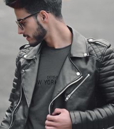 a man wearing glasses and a leather jacket is looking at his cell phone while standing in the street