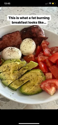 a white plate topped with meat, tomatoes and avocado on top of a table