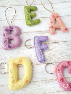 four felt letter ornaments hanging from hooks on a white wooden surface