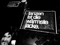 black and white photograph of a man holding up a sign that says tanzen ist die wamste jacke