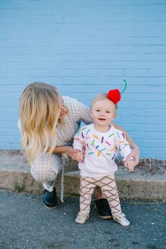 a woman holding a baby in front of a blue wall with an ice cream cone on it's head