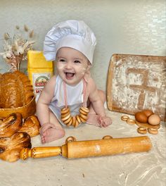 a baby sitting on the floor next to bread and doughnuts with a chef's hat