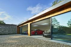 two cars are parked in the garage with glass doors on each side and one is red