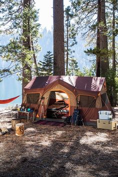 a tent is set up in the woods with hammock and coolers around it