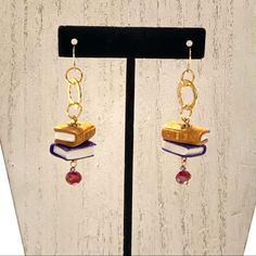 a pair of earrings with books and beads hanging from them