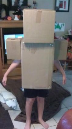 a young boy is standing on the floor with a cardboard box on his head and legs