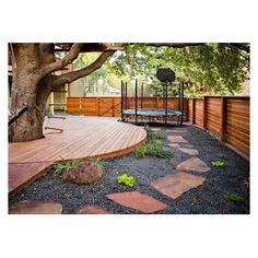 a wooden deck surrounded by rocks and trees with a swing set in the background on a sunny day