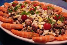 a platter filled with lobsters, tomatoes and other food on top of a table