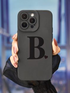 a person holding up a black phone case with the letter b on it in front of their face