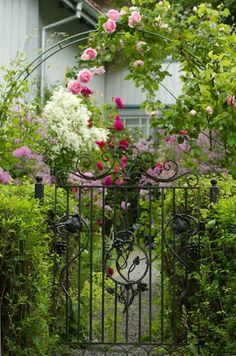 an iron gate with pink and white flowers growing on the top, in front of a house