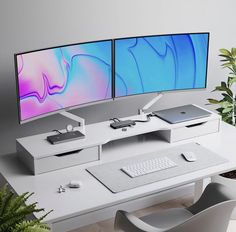 two computer monitors sitting on top of a white desk next to a potted plant