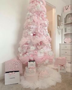 a pink christmas tree decorated with white and pink flowers, bows and other decorations in a room