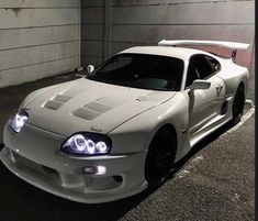 a white sports car parked in a parking lot next to a garage door and wall