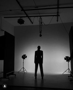 a man standing in front of three lights on a black and white photo shoot with his back to the camera