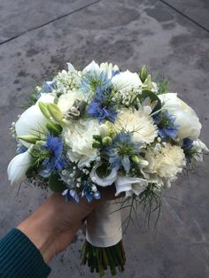 a bouquet of white and blue flowers is held by a person's hand on the sidewalk