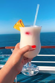 a hand holding up a drink on the deck of a cruise ship in the ocean