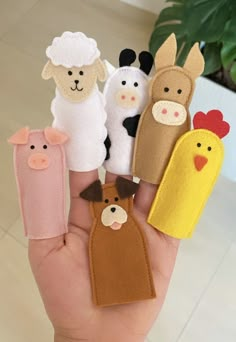 a hand holding five finger puppets with farm animals and chickens on them, all made out of felt