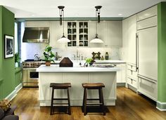 a kitchen with two stools in front of an island and green painted walls behind it