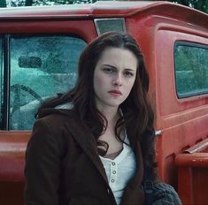 a woman standing in front of an old red truck with her hand on the door